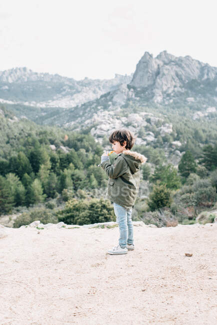 Pequeño niño curioso en abrigo caminando por la ladera rocosa explorando la naturaleza - foto de stock
