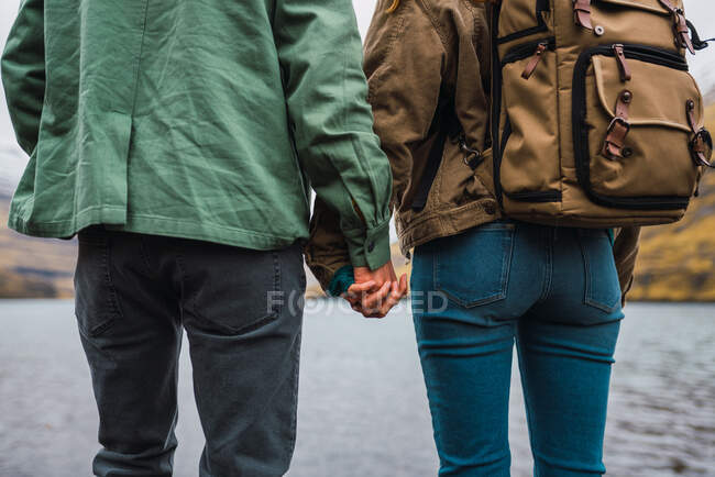 Vista trasera de una pareja cogida de la mano frente a un lago en la isla de Feroe - foto de stock