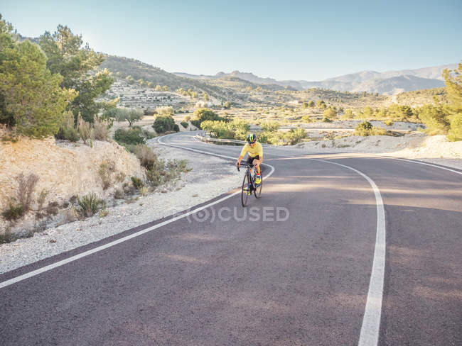 Healthy man riding bicycle on mountain road in sunny day — Stock Photo
