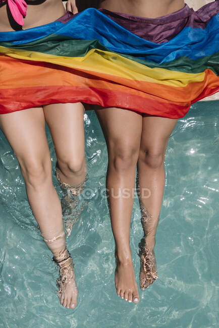 From above unrecognizable barefoot girlfriends with LGBT flag — Stock Photo