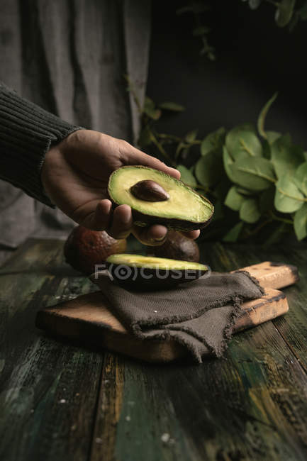 Человеческая рука держит половину авокадо над деревянным столом — стоковое фото