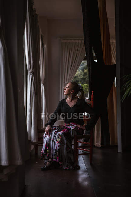 Приваблива вдумлива жіноча танцівниця в квіткової спідниці для фламенко сидячи і дивився вікно — стокове фото
