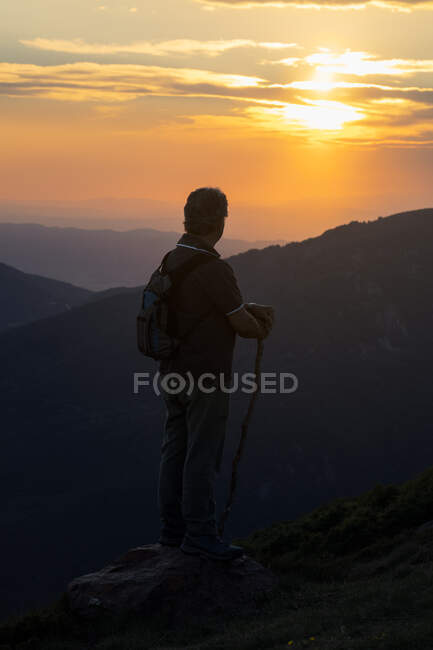 Silhueta de vista traseira de um homem sênior com mochila e madeira vara caminhadas contemplando incrível paisagem montanhosa — Fotografia de Stock