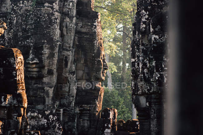 Antico monumento in pietra con volto sculture in parete illuminato con luce solare, Thailandia — Foto stock