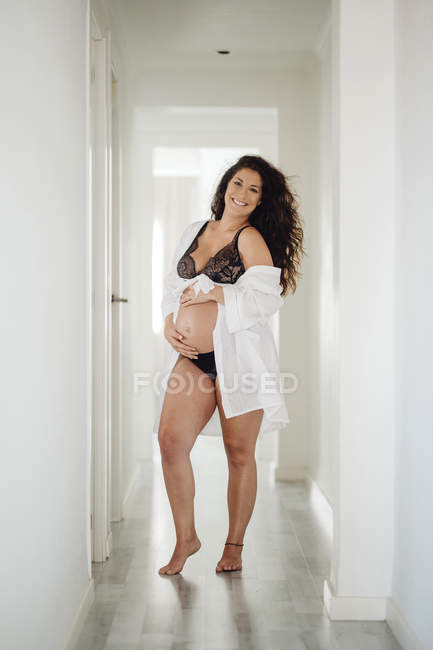 Mujer embarazada feliz en ropa interior de pie en casa - foto de stock