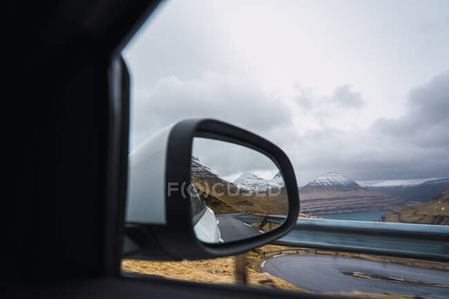 Carro moderno andando ao longo da estrada de asfalto em meio a colinas gramadas no dia nublado nas Ilhas Faroé — Fotografia de Stock