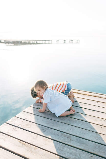 Adorable curious boy with toddler sister sitting on pier observing nature — Stock Photo