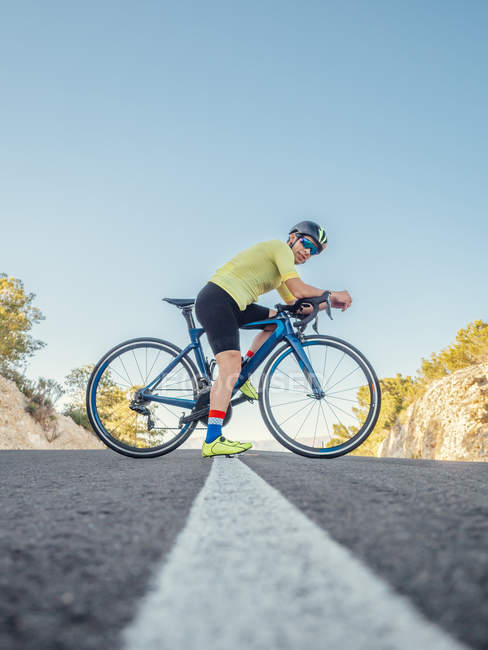 Homme en bonne santé se reposant debout avec vélo sur la route de montagne dans la journée ensoleillée — Photo de stock