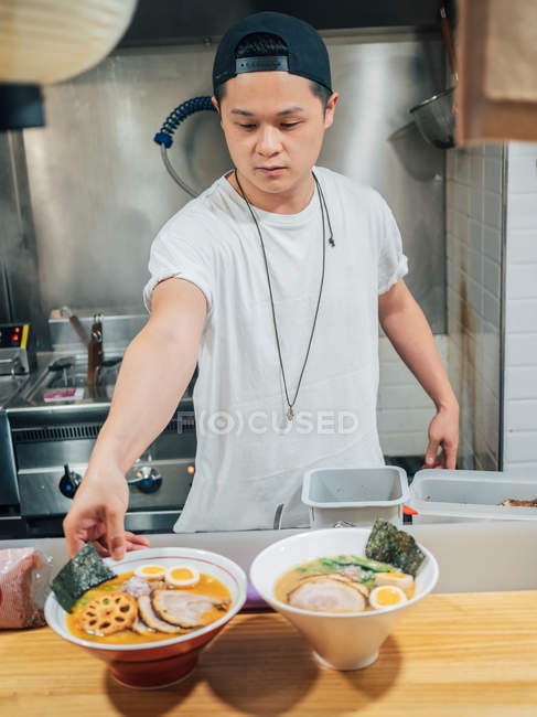 Junger Mann stellt Schüsseln mit frisch gekochtem traditionellem japanischem Gericht auf Holztheke im Restaurant — Stockfoto