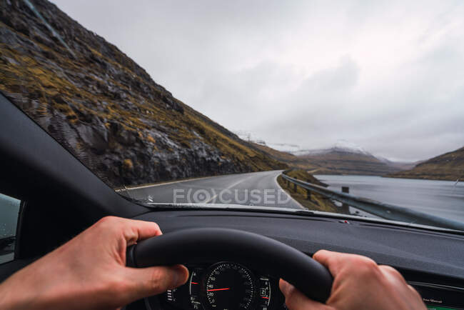 De l'intérieur d'une vue de voiture d'une personne anonyme conduisant une voiture dans une journée de pluie avec un fond de montagne enneigée — Photo de stock
