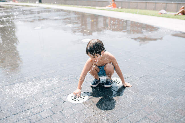 Маленький хлопчик у купальниках згинається біля струменя води виплескає з фонтану на вулиці — стокове фото