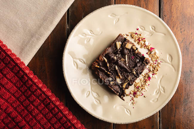 Сверху аппетитный ароматный коричневый торт с овсяными хлопьями в белой украшенной тарелке на деревянном фоне — стоковое фото