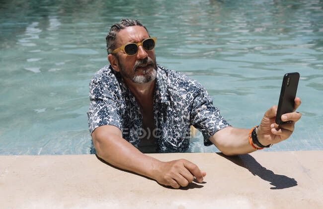 Старший чоловік використовує смартфон у басейні — стокове фото