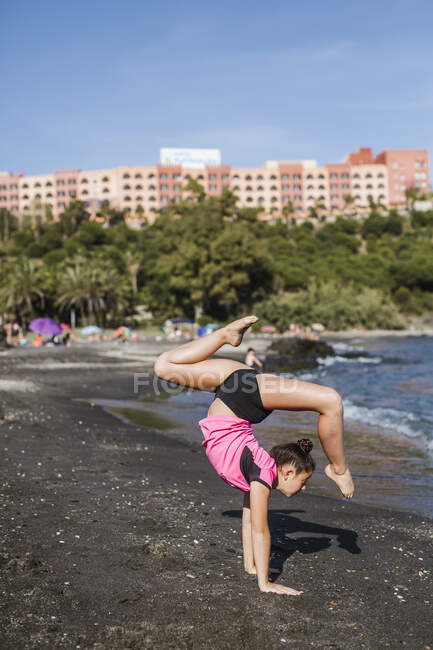 Vista laterale della giovane donna flessibile in piedi in posizione yoga sulla riva del mare nella giornata di sole — Foto stock