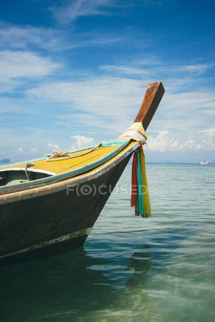 Tradizionale barca in legno con tessuto colorato galleggiante in acqua trasparente increspata sulla riva del mare, Thailandia — Foto stock