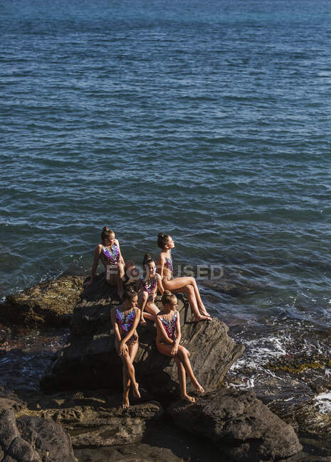 Graceful female athletes sitting by water on seashore and sunbathing on summer day — Stock Photo