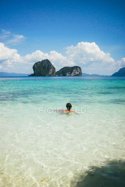 Back view of person lounging in peaceful clear water of ocean against blue sky, Thailand — Stock Photo