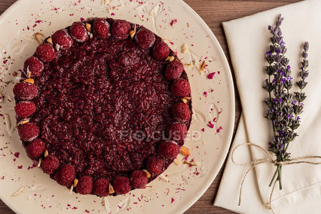 Sliced juicy fruit cake with raspberries on white plate on wooden table decorated with lavender bouquet — Stock Photo