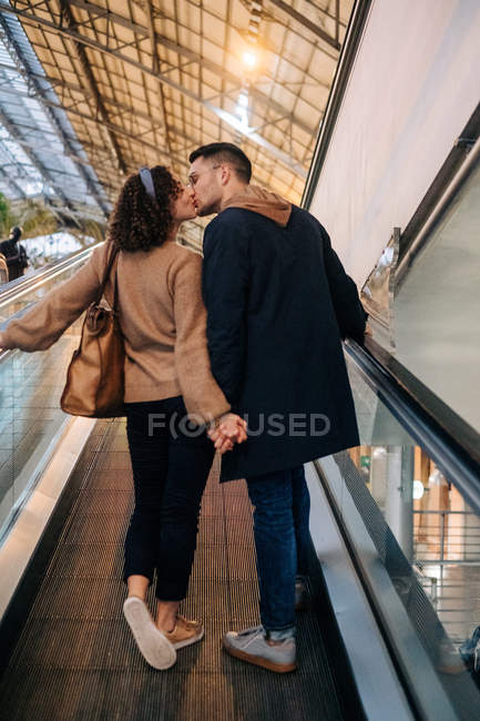 Вид ззаду молода людина і жінка тримаються за руки і цілуються, стоячи на прогулянці під час побачення в яскраво освітленому торговому центрі — стокове фото