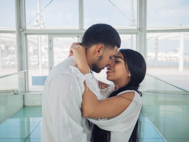 Вид збоку мила молода пара в легкому одязі зв'язаний і цілується з любов'ю і ніжністю в приміщенні — стокове фото
