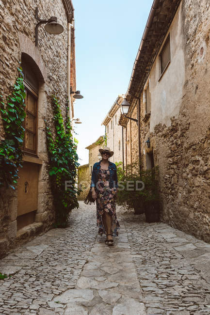 Mujer en vestido y sombrero caminando por la calle de la ciudad medieval - foto de stock