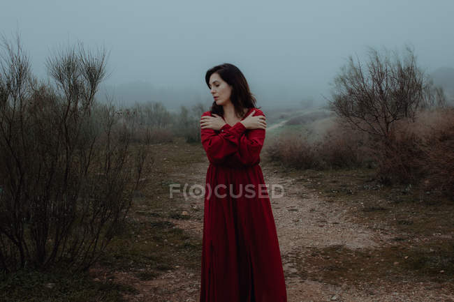 Мрійлива жінка в червоній сукні, що йде порожньою дорогою зруйнованої таємничої місцевості — стокове фото