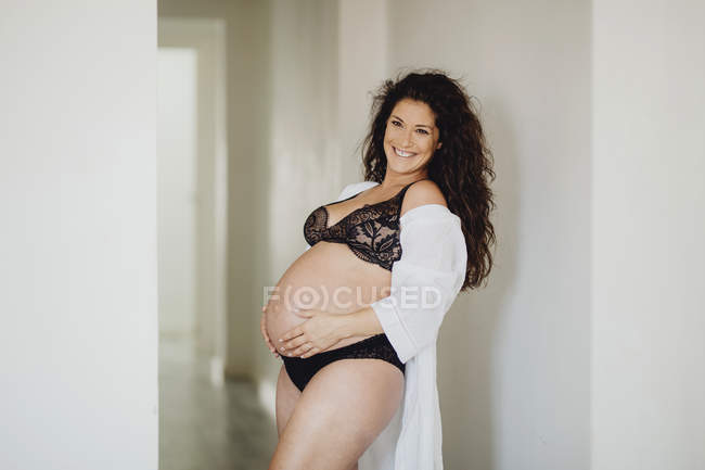 Mujer embarazada feliz en ropa interior y albornoz de pie en casa - foto de stock