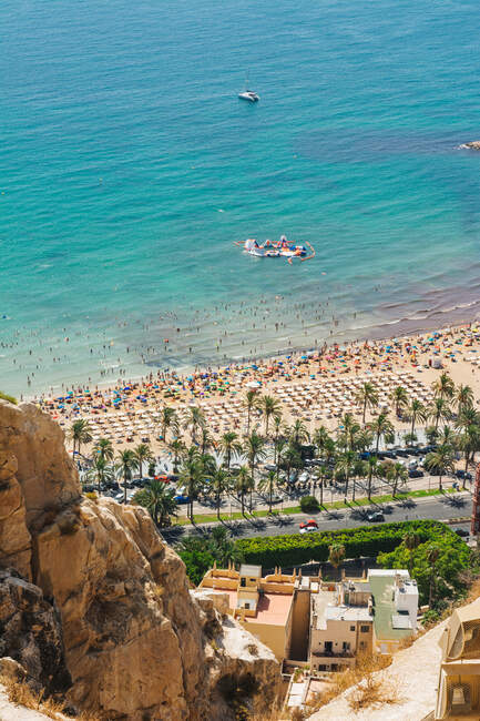 Desde lo alto impresionante paisaje de mar turquesa sereno y playa tentadora con gente de palma barcos en Alicante España - foto de stock