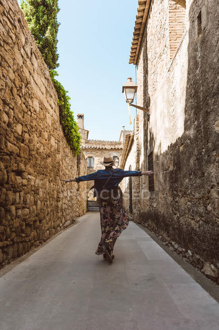 Donna in abito e cappello che tende le braccia sulla strada della città medievale — Foto stock
