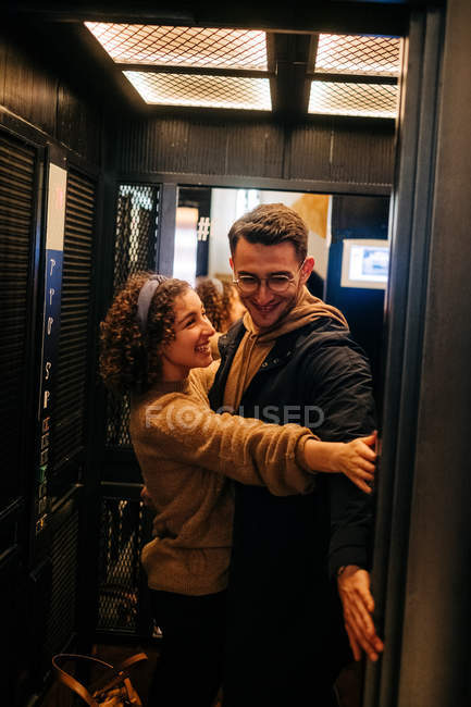 Side view of cheerful young man and woman holding door of elevator and smiling during romantic date — Stock Photo