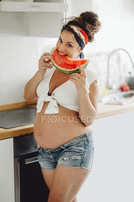 Donna incinta mangiare deliziosa anguria e sorridente alla fotocamera — Foto stock