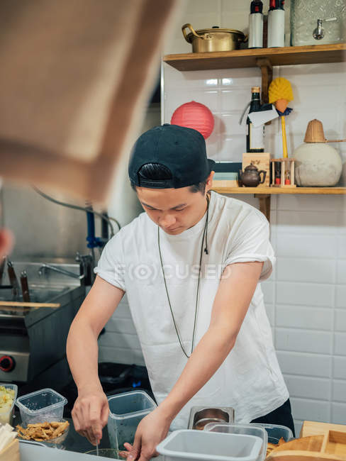 Jeune homme en t-shirt blanc et chapeau noir cuisine ramen au restaurant japonais — Photo de stock