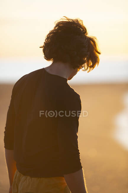 Ragazzo premuroso che cammina sulla spiaggia di sabbia alla sera del tramonto — Foto stock