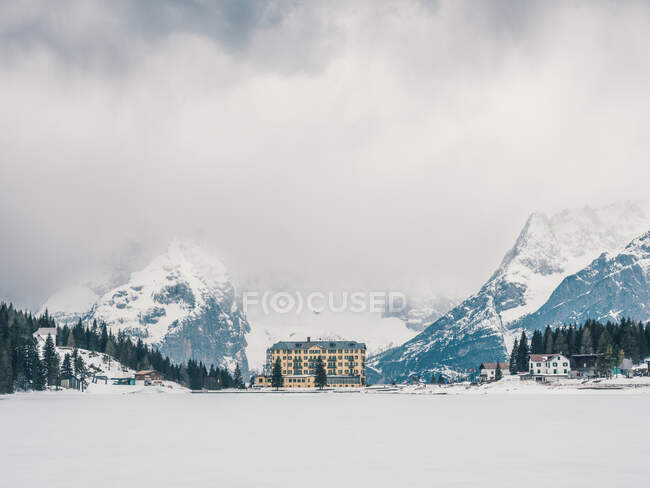 Bright multi-store building standing in snowy area on background of rocky mountains and dense forest — Stock Photo