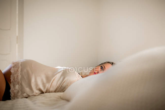 Беременная женщина в нижнем белье расслабляется на удобной кровати дома — стоковое фото
