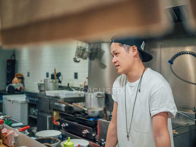 Junger Mann in weißem T-Shirt und schwarzer Mütze kocht Ramen in japanischem Restaurant — Stockfoto