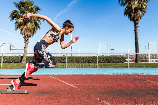 Strong female athlete in sportswear running fast against blue sky on sunny day on stadium — Stock Photo