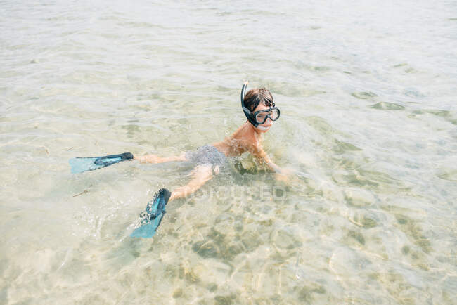 Мальчик в ластах и маске для дайвинга во время плавания и исследования дна на мелководье — стоковое фото