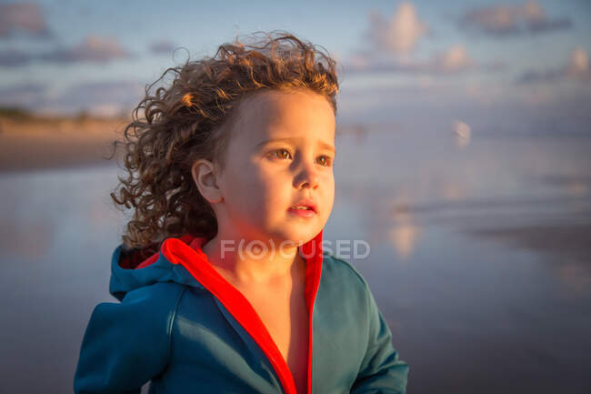 Кудрявый ребенок в полосатой прогулке по пляжу на размытом фоне природы — стоковое фото