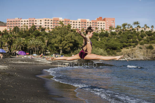 Professional gymnast in jump on seashore — Stock Photo