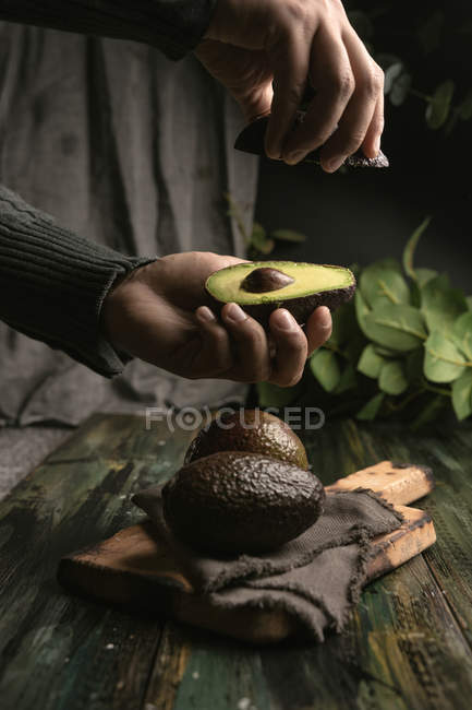 Mani umane che tengono avocado dimezzato su tavolo di legno — Foto stock