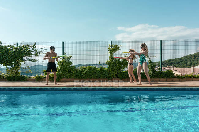 Amigos jugando con pistolas de agua en la piscina en un soleado día de verano. - foto de stock