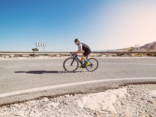 Uomo sano in bicicletta su strada in giornata di sole con paesaggio arido sullo sfondo — Foto stock