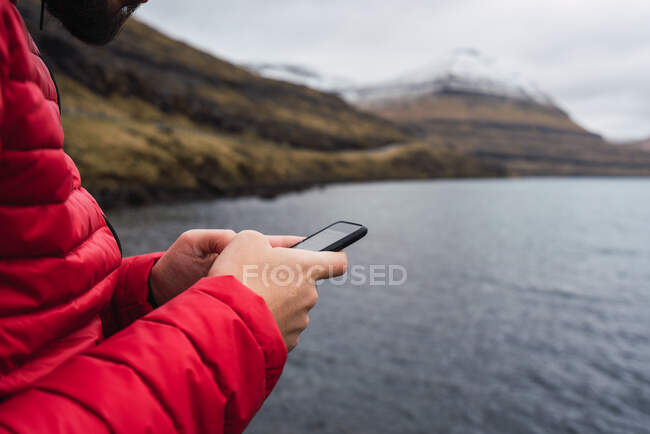 Uomo anonimo che utilizza smartphone vicino a un lago nell'isola di Faroe — Foto stock