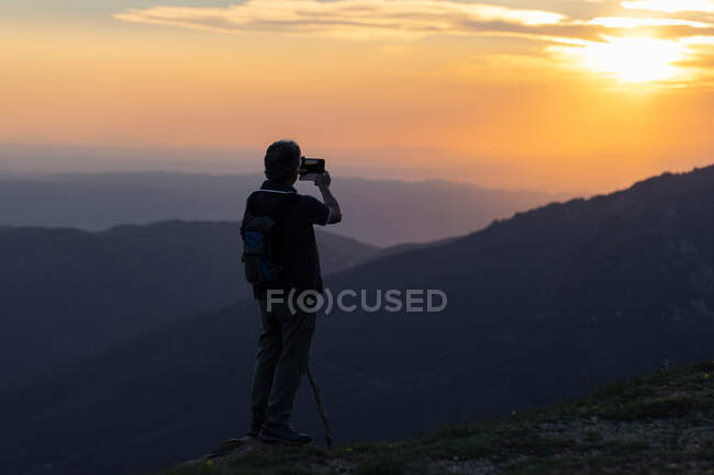 Rückansicht eines älteren Mannes, der mit dem Handy fotografiert, während er die atemberaubende Berglandschaft betrachtet — Stockfoto