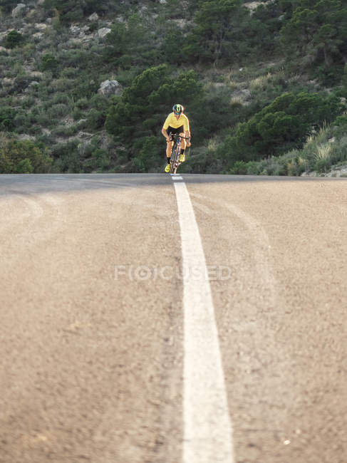 Healthy man riding a bicycle on mountain road in sunny day — Stock Photo