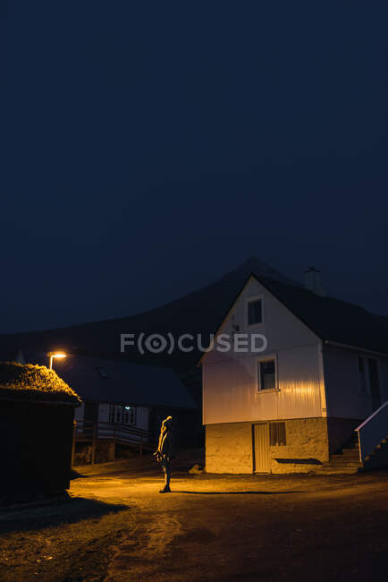 Frau schaut nachts in einer Straße eines kleinen Dorfes mit Licht auf der Insel Färöer auf — Stockfoto