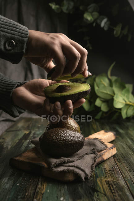 Людські руки тримають половину авокадо над дерев'яним столом — стокове фото