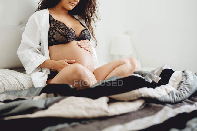 Closeup of expecting baby sitting on bed at home — Stock Photo
