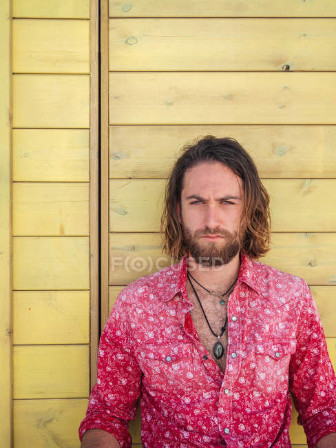 Confident bearded man in casual outfit sitting against yellow wall on resort — Stock Photo